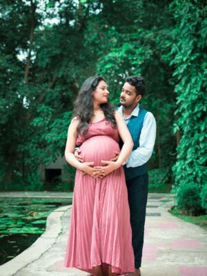 A joyful pregnant couple embracing outdoors, capturing love and anticipation in a garden.