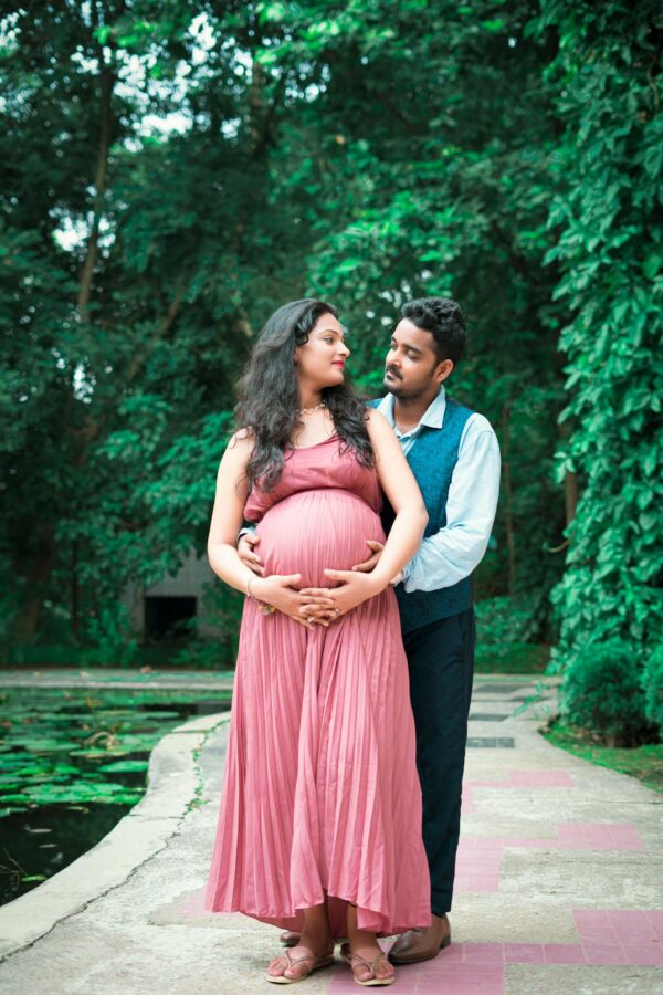 A joyful pregnant couple embracing outdoors, capturing love and anticipation in a garden.