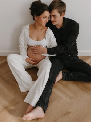 A loving couple sits barefoot on the floor, celebrating pregnancy with joy and intimacy.