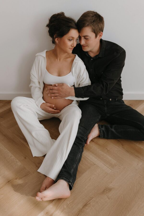 A loving couple sits barefoot on the floor, celebrating pregnancy with joy and intimacy.