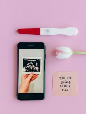 Flat lay of pregnancy test, ultrasound, and message on pink background.