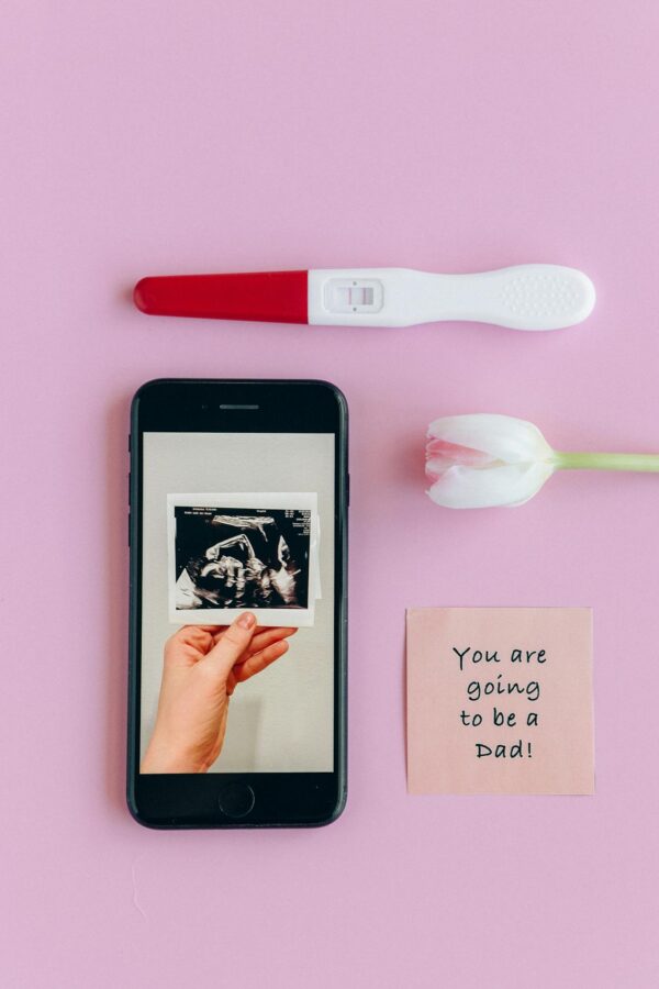 Flat lay of pregnancy test, ultrasound, and message on pink background.