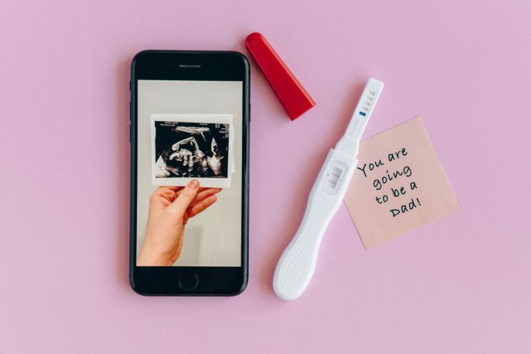 Pink background with a pregnancy test, ultrasound image, and a note for a dad-to-be.