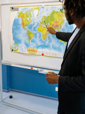 Teacher pointing at world map in classroom setting, emphasizing global geography.